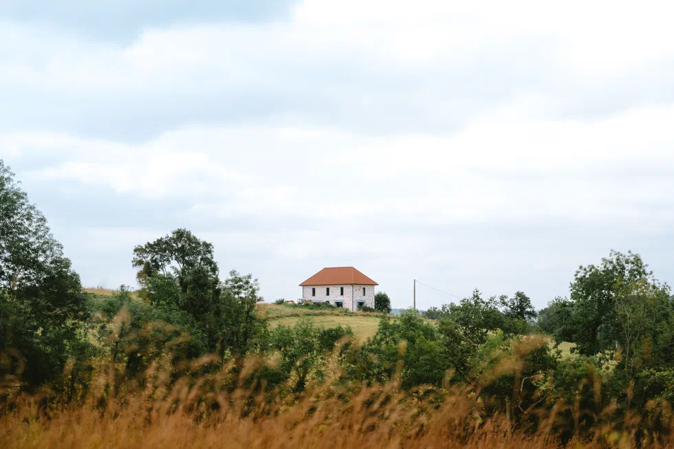 Maison isolée sur une colline entre arbres et herbes hautes