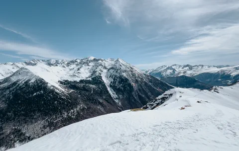 Panoramique des montagnes recouvertes de neige, avec des cimes majestueuses se détachant contre un ciel clair, créant un paysage hivernal impressionnant.