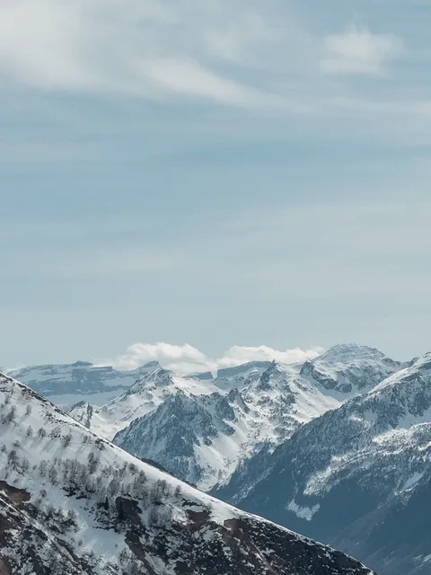 Vue splendide des montagnes enneigées depuis le sommet, avec des vallées profondes et des crêtes enneigées à perte de vue, capturant la beauté sauvage et paisible de la nature.