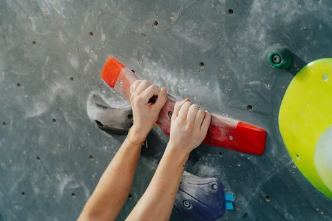 Deux mains agrippent une grande prise rouge sur un mur d’escalade